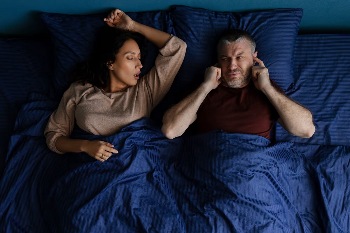 Woman snoring while her partner covers his ears in bed
